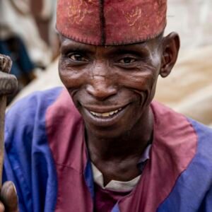 Portrait of a joyful man in Kaduna, Nigeria, wearing traditional attire and cap.
